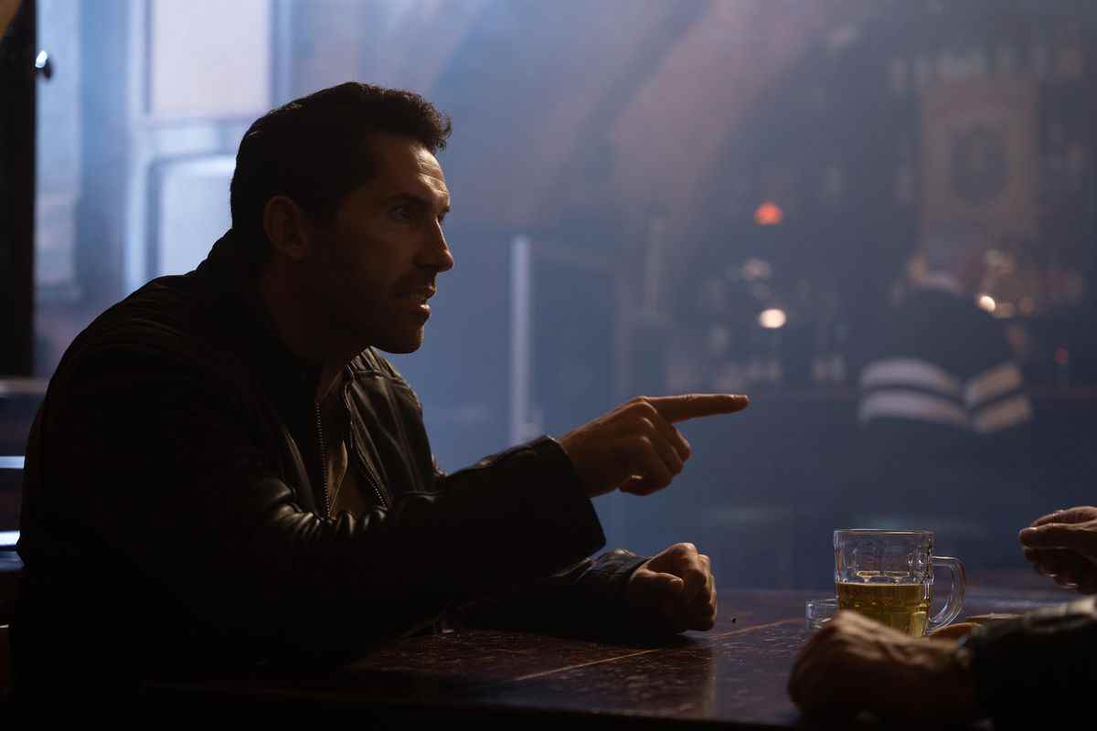 Scott Adkins pointe son doigt alors qu'il est assis à une table de bar dans Accident Man: Hitman's Holiday