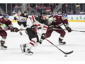 Le Canadien Ridly Grieg (17) est poursuivi par le Letton Peteris Purmalis (20) et Bogdans Hodass (17) lors de la deuxième période du Championnat mondial de hockey junior de l'IIHF à Edmonton le mercredi 10 août 2022.