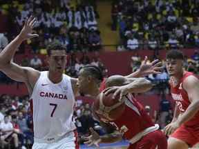 Le Panama Trevor Gaskins, au centre, dribble le ballon contre le Canadien Dwight Powell, à gauche, lors d'un match de qualification de basket-ball WCup America à l'arène Roberto Duran de Panama City, le lundi 29 août 2022.