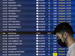 Une personne passe devant un tableau des départs rempli d'avis de retard au terminal 1 de l'aéroport international Pearson de Toronto, le 7 juillet 2022.