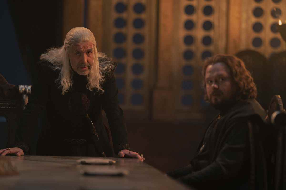 le roi Viserys et Lord Strong à la table du petit conseil ;  Viserys est debout et regarde vers le haut, tandis que Viserys est assis et tourné pour regarder de la même manière 