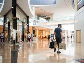 Un client sort d'un magasin contenant plusieurs sacs à provisions dans le centre commercial Sherway Gardens à Toronto.