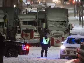 Un agent de la Police provinciale de l'Ontario tient un barrage routier le long de la rue Wellington, alors qu'un avertissement de tempête hivernale était en vigueur, le 22e jour d'une manifestation contre les mesures COVID-19 qui s'était transformée en une manifestation antigouvernementale plus large à Ottawa le vendredi 22 février. 18, 2022.