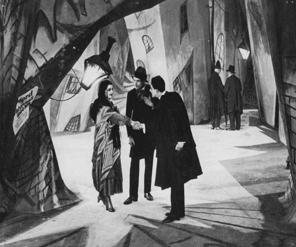 Trois personnages se tiennent au centre d'une intersection dentelée dans Le Cabinet du Dr Caligari de Robert Weine.