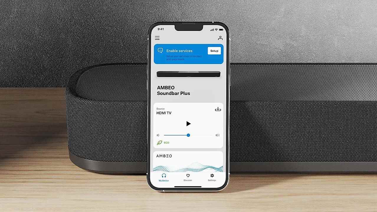 image aux trois quarts montrant la Sennheiser Ambeo Soundbar Plus sur une surface en bois avec l'application affichée sur le smartphone