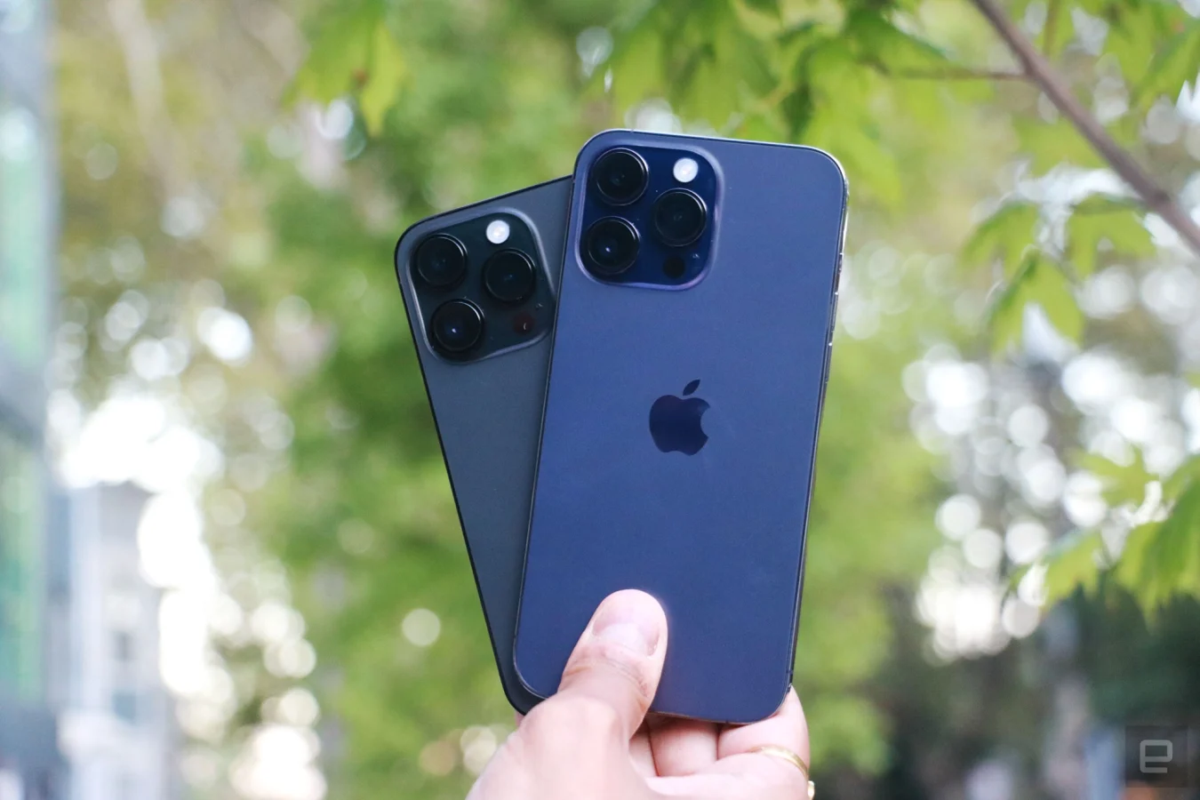 L'iPhone 14 Pro Max violet et l'iPhone 14 Pro noir se tiennent l'un sur l'autre dans une main, légèrement déployés pour que vous puissiez voir les triples caméras arrière de chaque combiné.