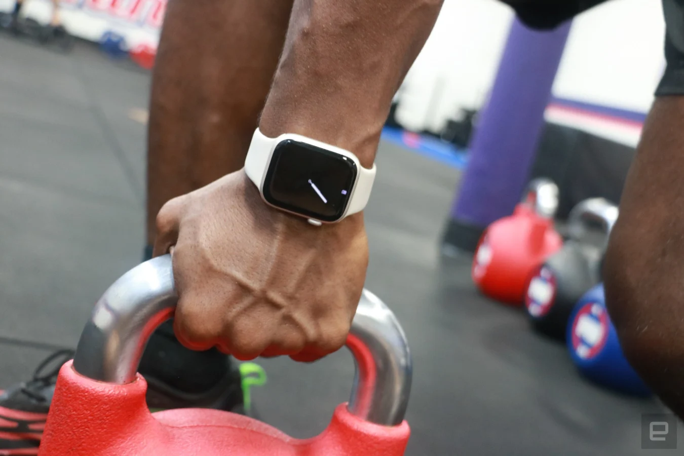 Une Apple Watch Series 8 au poignet d'une personne tenant une kettlebell rouge, montrant son affichage permanent.