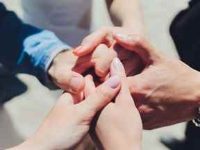 deux hommes et trois femmes se tenant la main sur une table impliquant une relation polyamoureuse ou un triangle amoureux.