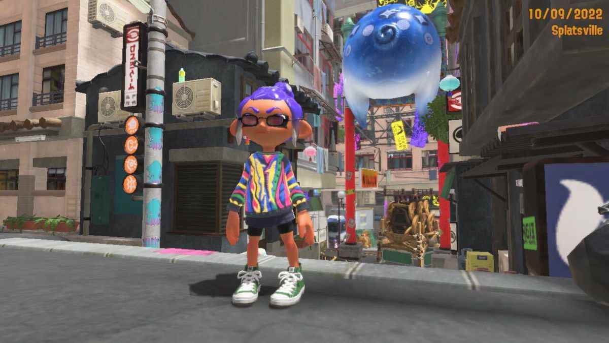 Un Octaling aux cheveux violets se tient dans le quartier de Splatsville de Splatoon 3. L'Octaling porte un pull coloré, des lunettes de soleil élégantes et des chaussures montantes vertes.