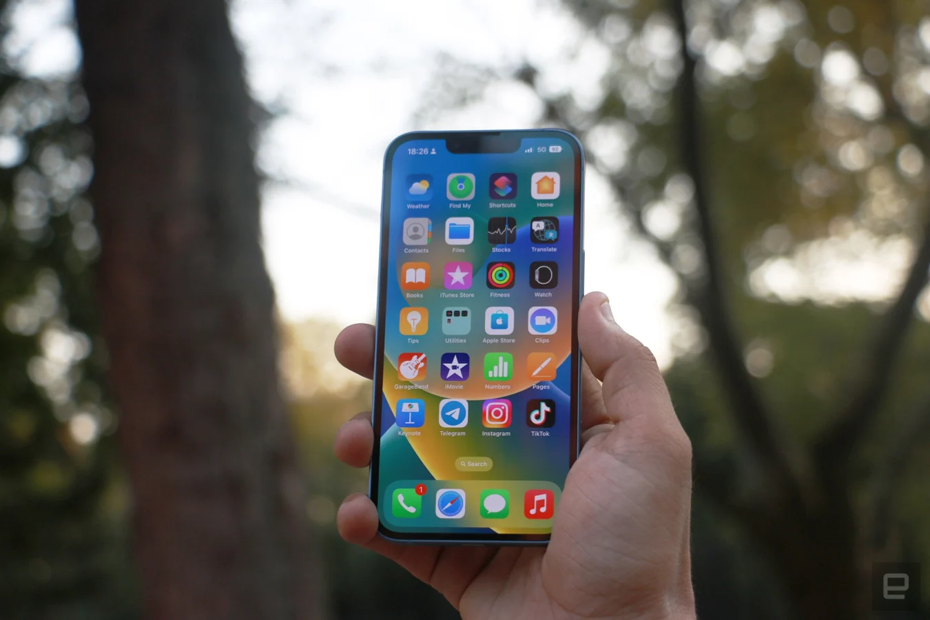 L'iPhone 14 tenu en l'air devant des arbres avec la page d'accueil iOS vers l'extérieur.