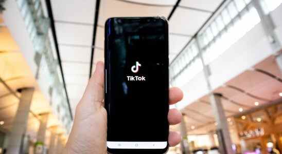 Hand of man holding mobile phone opening Tik Tok application, in shopping mall.