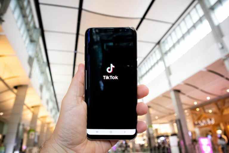 Hand of man holding mobile phone opening Tik Tok application, in shopping mall.