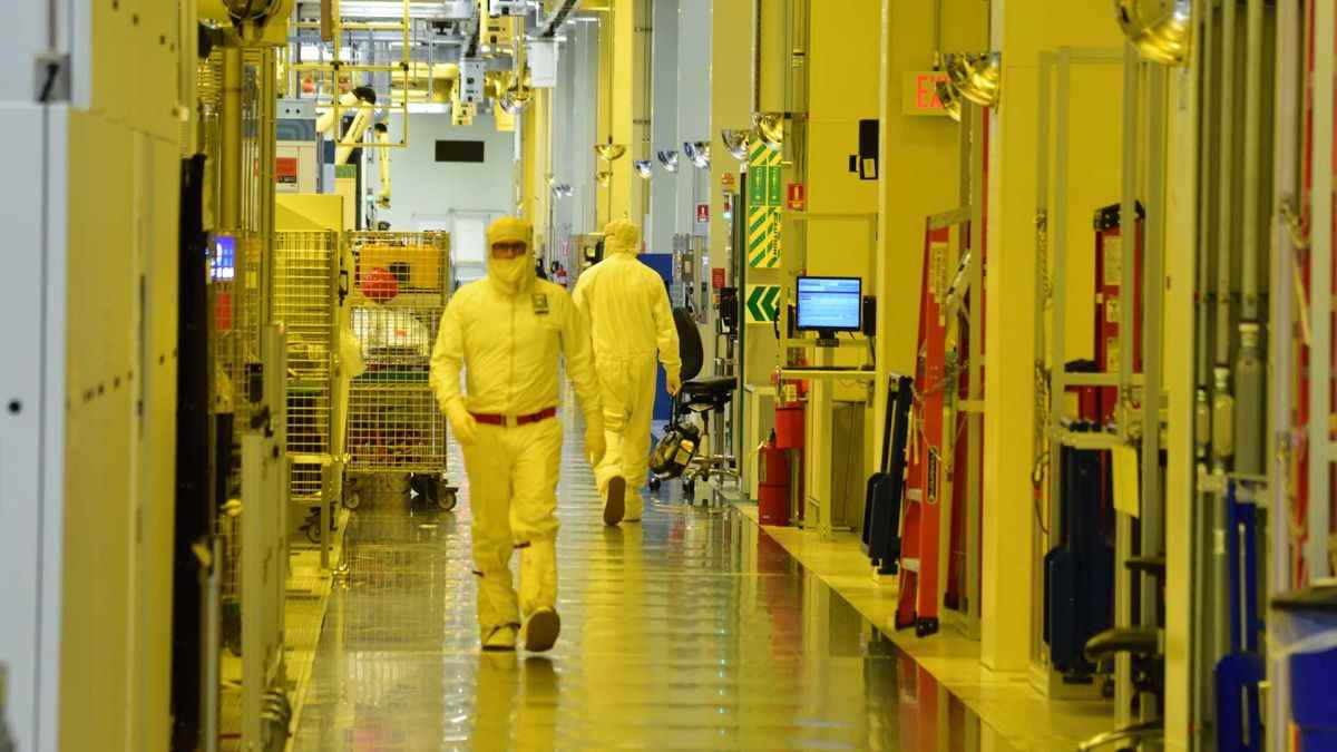 Photograph taken inside an Intel semiconductor fabrication plant showing person in overalls (bunny suit) walking past lithographic equipment.