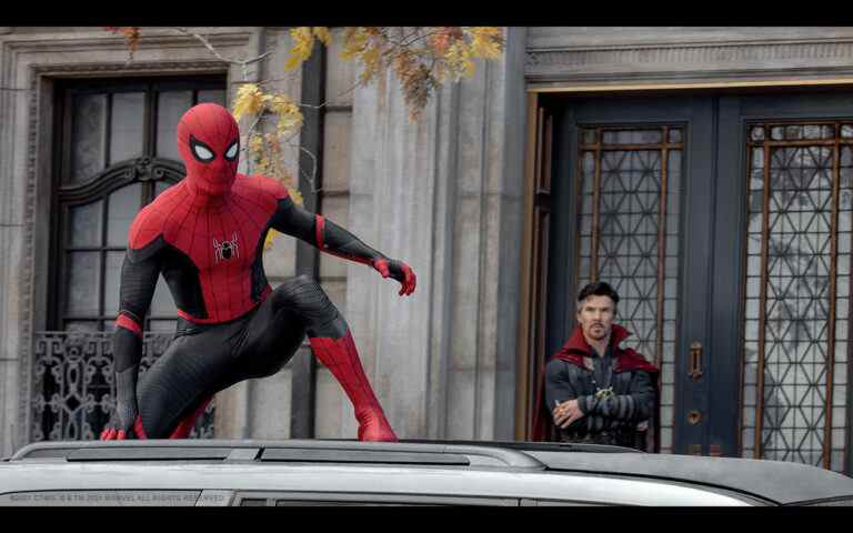 Spider-Man crouches on top of a car while Dr. Strange looks on with his arms crossed