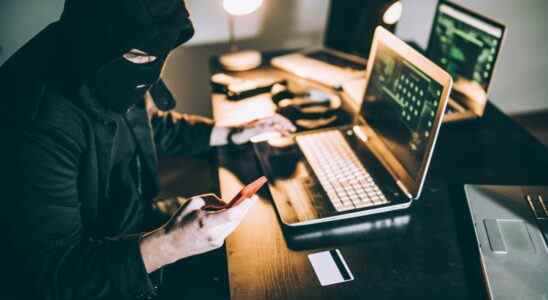 Hacker using a phone and pc while wearing a ski mask.