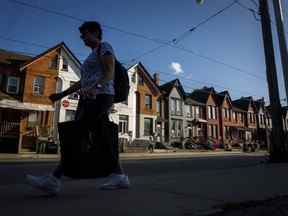 Une personne passe devant une rangée de maisons à Toronto, le 12 juillet 2022. L'allégement de l'inflation récemment annoncé par le gouvernement fédéral pour les Canadiens à faible revenu grâce au remboursement de la taxe sur les produits et services constitue une meilleure politique que certains des paiements en espèces émis par les provinces, disent les économistes.