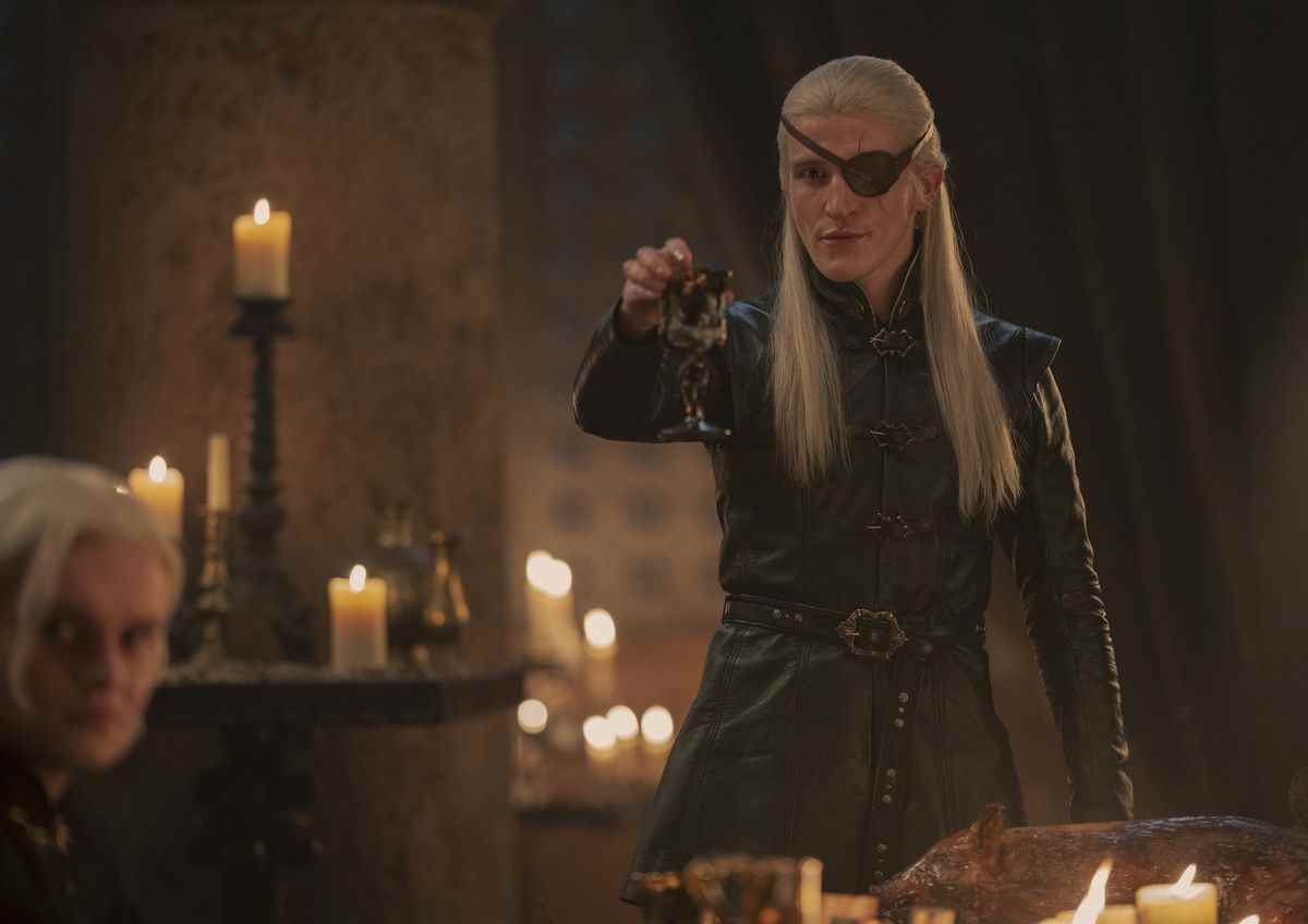 Ewan Mitchell dans le rôle d'Aemond Targaryen dans House of the Dragon levant un verre en toast moqueur avec son cache-œil sur