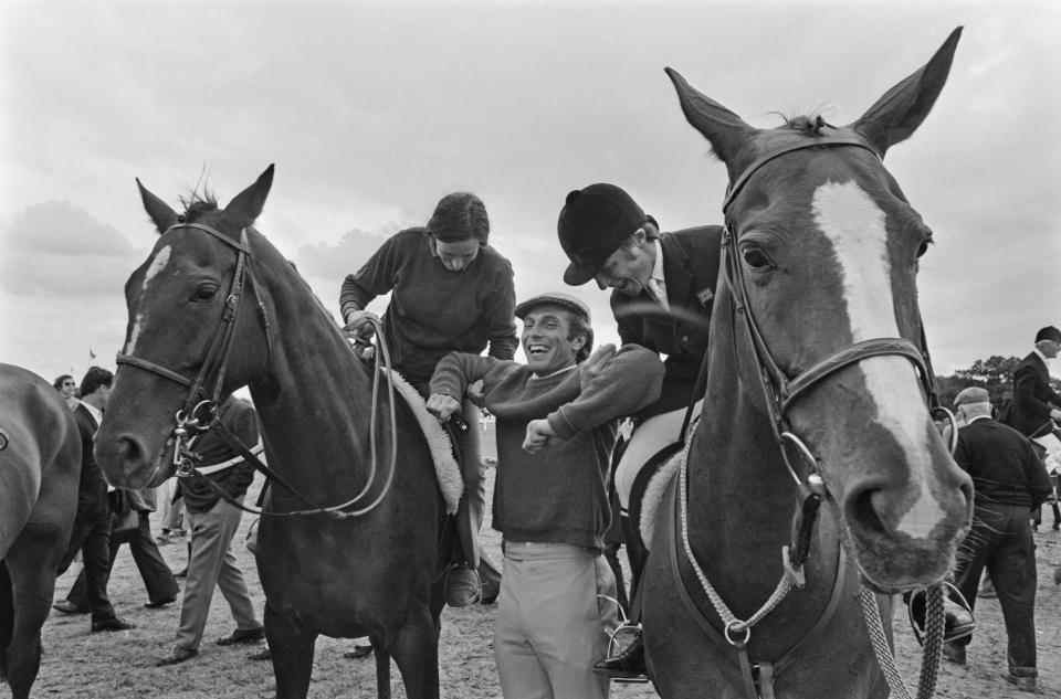 British Royal Anne, Princess Royal, habillée en tenue d'équitation alors qu'elle est assise à cheval, soulevant son fiancé, le capitaine équestre britannique Mark Phillips, avec un homme non spécifié, également à cheval, au All England Jumping Course à Hickstead, un centre équestre à West Sussex, Angleterre, juillet 1973. (Photo de McCarthy/Daily Express/Hulton Archive/Getty Images)