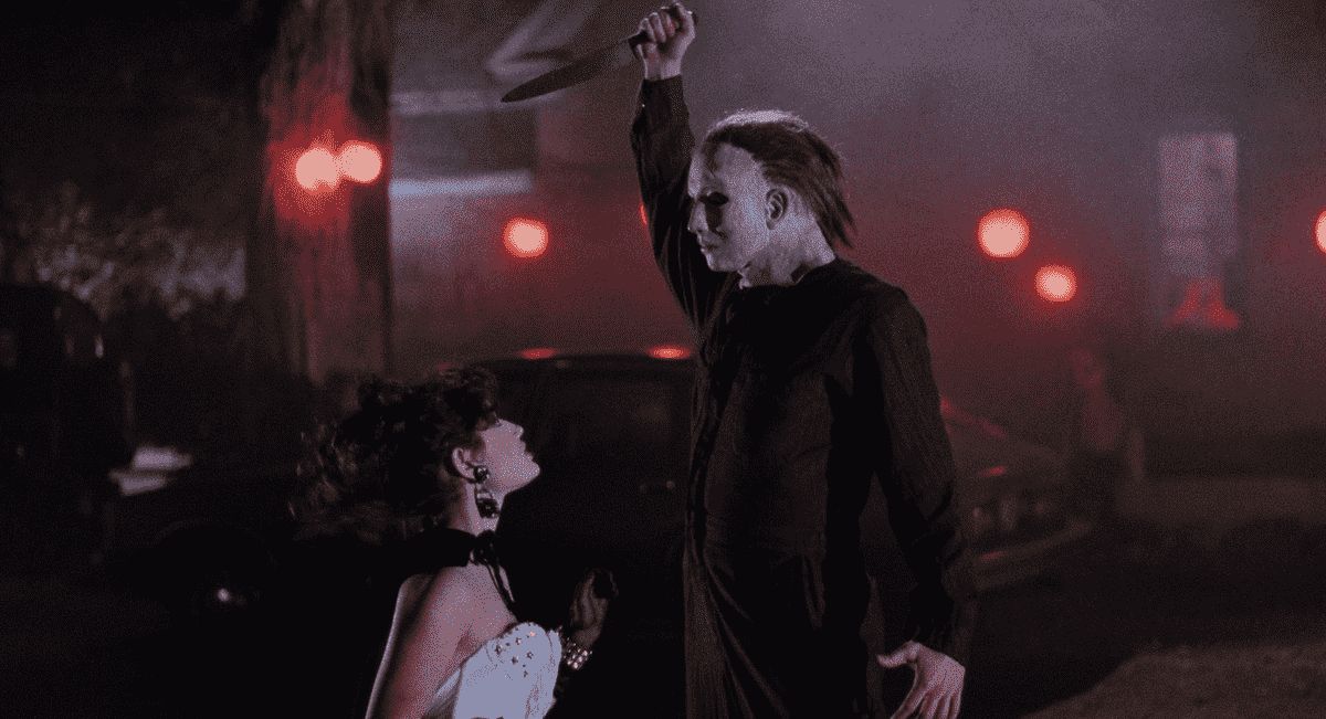 Un Michael Myers hirsute étend raidement son bras au-dessus de sa tête, prêt à poignarder une femme agenouillée en robe blanche, dans Halloween 5 : La Revanche de Michael Myers.