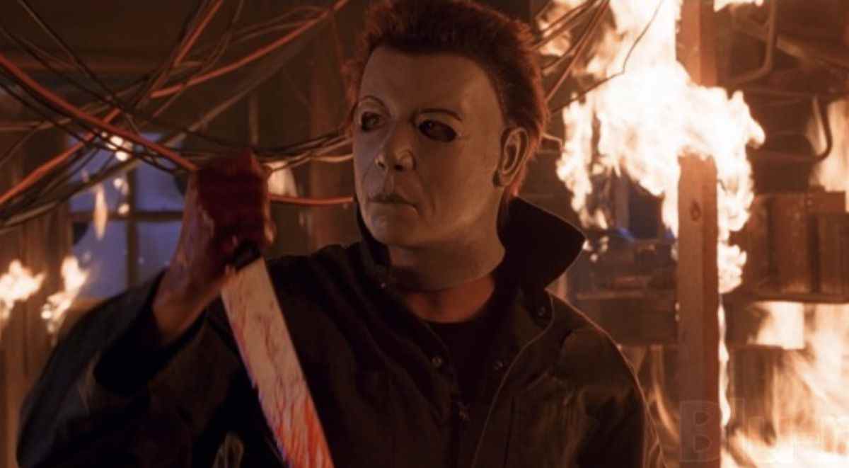 Michael Myers, entouré de flammes, porte un masque aux sourcils arqués et au nez plus distinct.  Il tient un couteau ensanglanté.