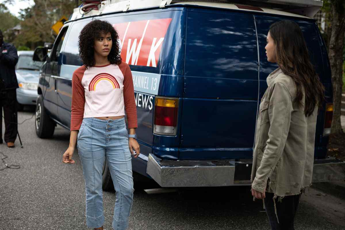 Jasmin Savoy Brown porte une chemise à manches longues avec un arc-en-ciel dessus et un jean devant un camion de presse dans Scream en 2022.