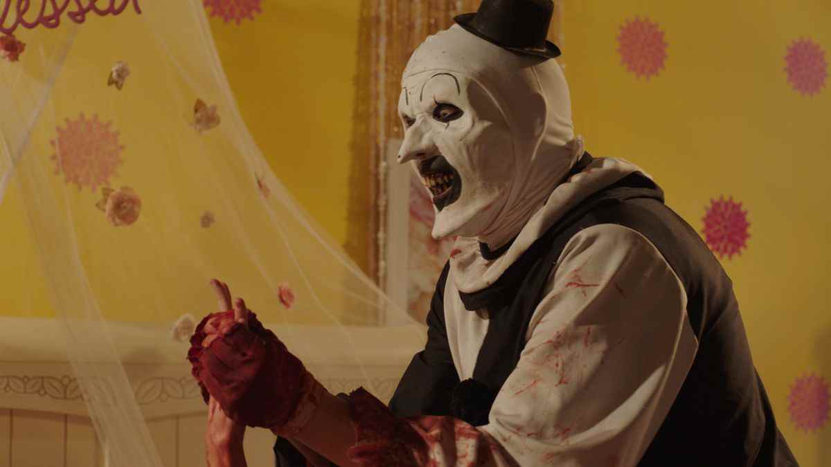 David Howard Thornton en tant que mime tueur Art the Clown traque une victime à travers une pièce jaune vif dans Terrifier 2