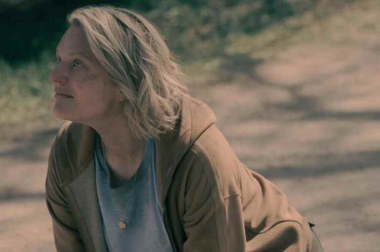 A blonde woman with bruises and cuts on her face, kneeling on a dirt road and looking up at someone O.S.; still from "The Handmaid's Tale"