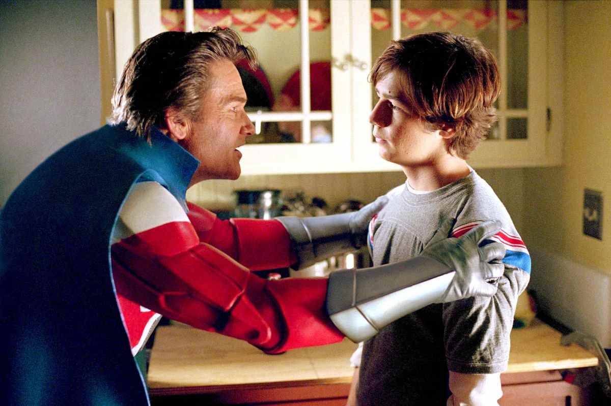 Kurt Russell dans son costume de super-héros tient un jeune Michael Angarano par les épaules dans Sky High