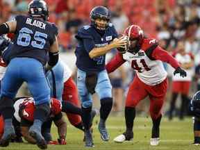 Le quart-arrière des Argonauts de Toronto McLeod Bethel-Thompson (4) tente d'échapper à un tacle du joueur de ligne défensif des Stampeders de Calgary Mike Rose (41) lors de la première mi-temps de l'action de football de la LCF à Toronto le samedi 20 août 2022. /