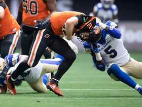 Le quart-arrière des Lions de la Colombie-Britannique Nathan Rourke (12 ans) est limogé par Willie Jefferson (5 ans) des Blue Bombers de Winnipeg au cours de la première mi-temps samedi soir.  (Daryl Dyck)