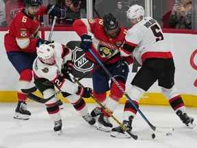 L'ailier droit des Sénateurs d'Ottawa Alex DeBrincat (12) et le défenseur Nick Holden (5) se battent pour la possession contre le défenseur des Panthers de la Floride Marc Staal (18) alors que le centre Colin White (6) regarde pendant la deuxième période au FLA Live Arena.