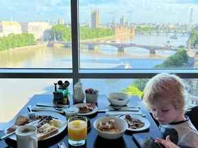 Garçon jouant sur l'appareil pendant qu'il apprécie le petit-déjeuner dans la chambre d'hôtel de Londres avec vue sur la ville.