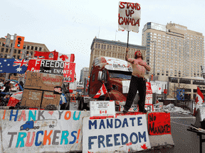 Des gens se tiennent devant des camions bloquant une rue du centre-ville alors que des camionneurs et leurs partisans protestent contre les restrictions liées à la COVID-19 à Ottawa, le 16 février 2022.