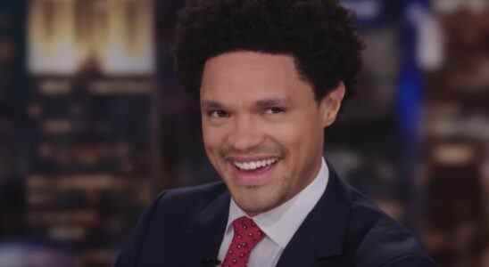 Trevor Noah smiling behind The Daily Show desk