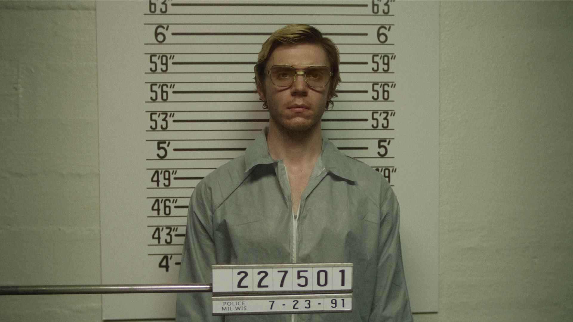 Jeffrey Dahmer d'Evan Peters se tient devant un mur de mesure alors que sa photo de police est prise dans Monster: The Jeffrey Dahmer Story