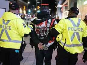 La police arrête une personne alors qu'elle travaillait pour nettoyer une zone de la rue Rideau, lors d'une manifestation de type convoi que les participants appellent "tonnerre roulant," à Ottawa, le vendredi 29 avril 2022. L'enquête publique sur l'utilisation sans précédent de la Loi sur les mesures d'urgence par le gouvernement fédéral lors de ce que les organisateurs ont appelé "Convoi de la liberté" les manifestations de l'hiver dernier commencent jeudi et 65 témoins, dont le premier ministre Justin Trudeau et des organisateurs de convois de haut niveau, devraient témoigner.