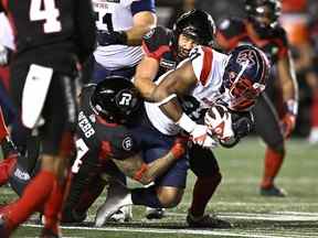 Le porteur de ballon des Alouettes William Stanback (31 ans) est plaqué par le secondeur du Rouge et Noir d'Ottawa Adam Auclair (32 ans) et le demi défensif Damon Webb (34 ans) lors de la deuxième mi-temps de la LCF à Ottawa le vendredi 14 octobre 2022.