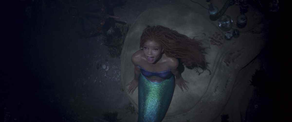 Halle Bailey avec la nageoire verte et les cheveux roux d'Ariel chantant tout en regardant du fond de l'océan dans La Petite Sirène