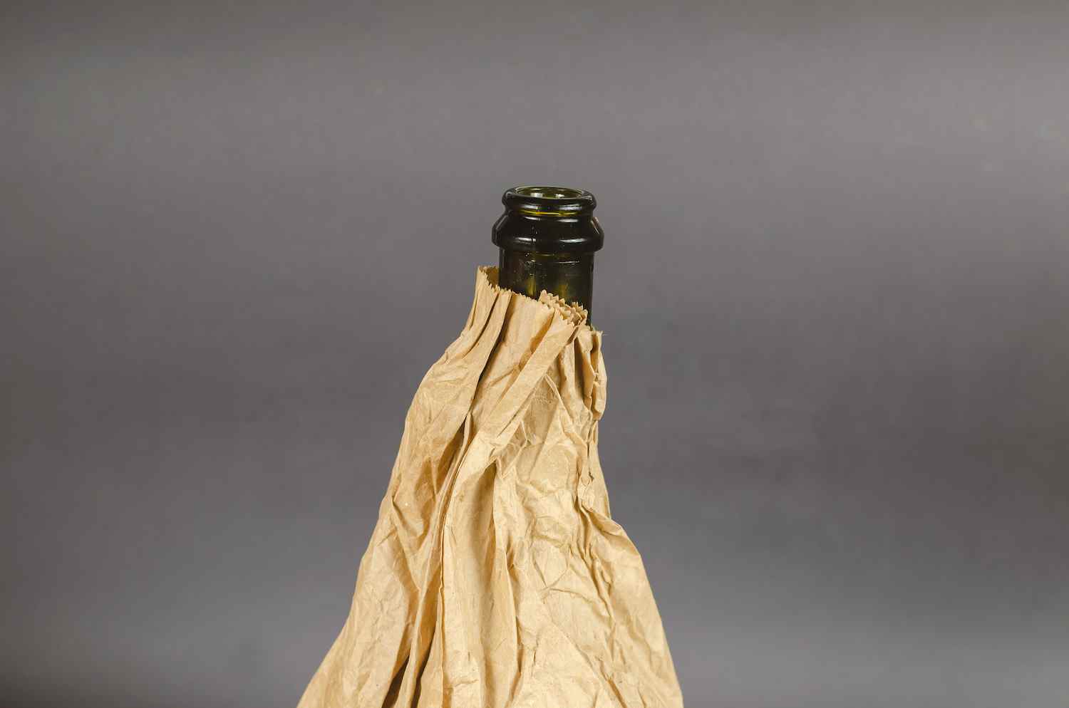 Bouteille dans un sac en papier sur fond gris.  Bouteille d'alcool sombre dans un sac marron froissé.  Fermer.  Mise au point sélective.