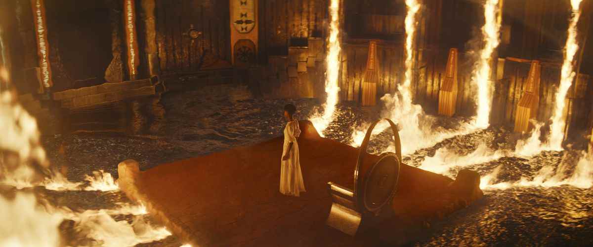 Shuri (Letitia Wright) se tient dans une salle du trône entourée de piliers de feu reflétés contre des flaques d'eau dans Black Panther : Wakanda Forever.