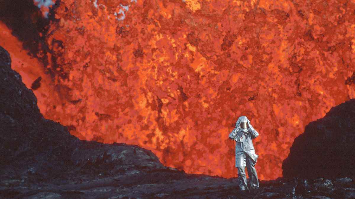 Une personne vêtue d'une combinaison ignifuge s'éloigne de la bouche d'un geyser débordant de lave.