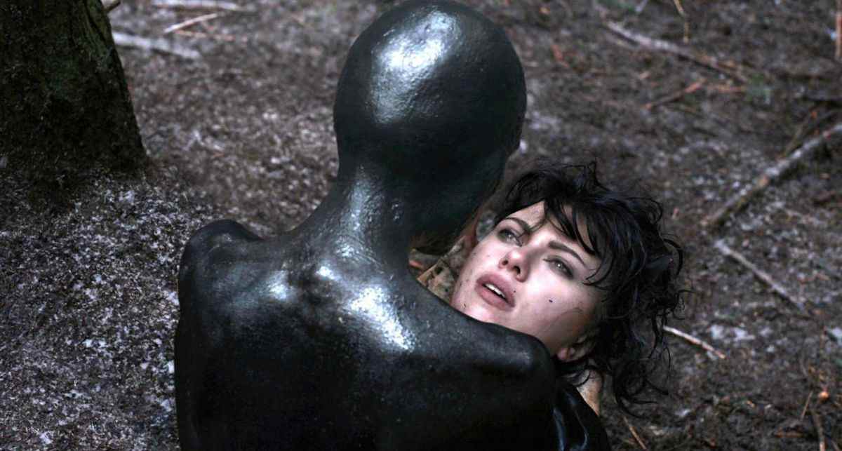 Une créature humanoïde noire tient un visage humain dans ses mains dans Under the Skin.