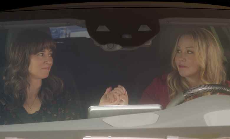 Two women holding hands in the front seat of a car; still from "Dead to Me"