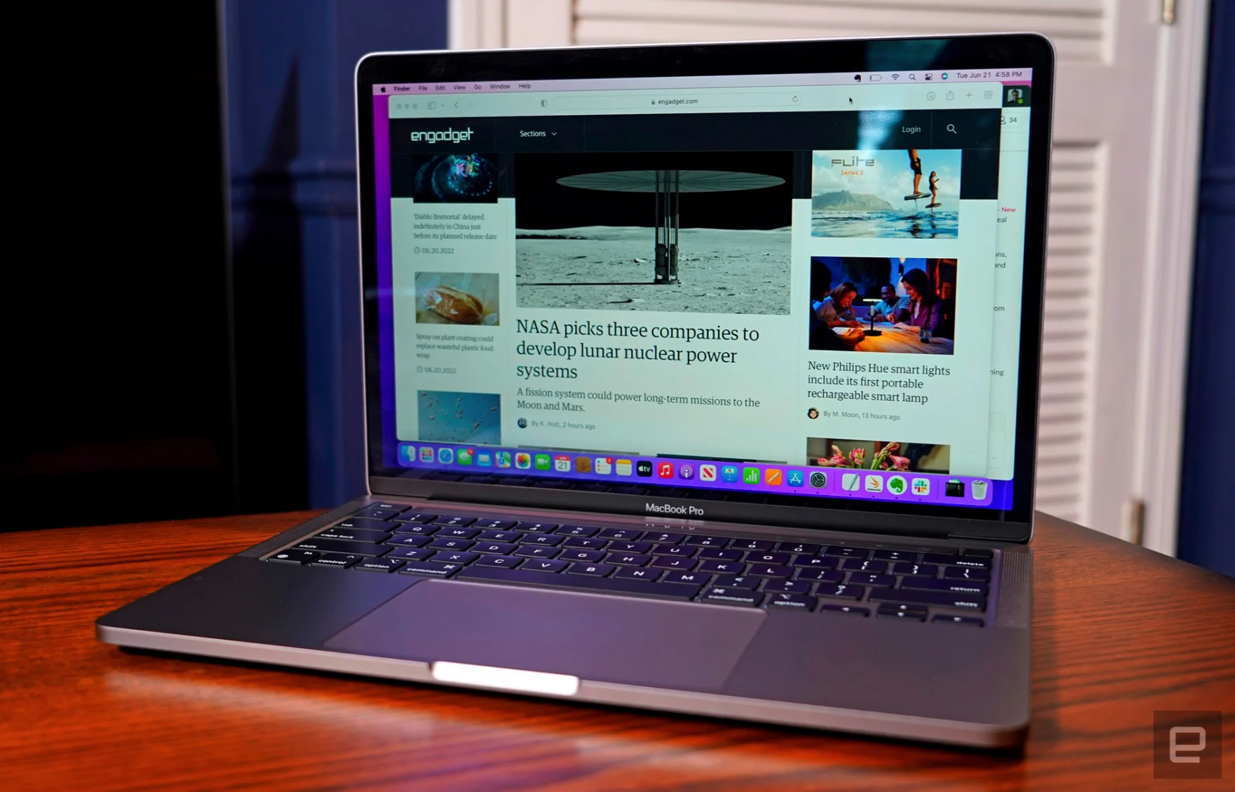 Le MacBook Pro 13 pouces M2 (2022) est ouvert sur une table de salle à manger en bois dans une pièce aux murs bleus et aux portes blanches.