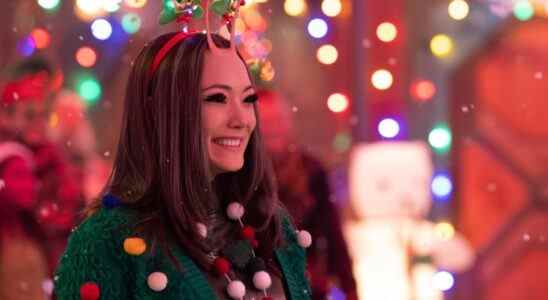 A female-presenting alien with mid-length dark hair, large eyes, and two insect-like antennae, smiling as she wears a green holiday sweater while surrounded by twinkling lights; still from "The Guardians of the Galaxy Holiday Special."