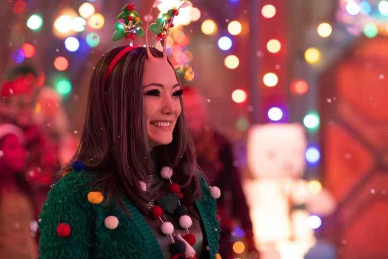 A female-presenting alien with mid-length dark hair, large eyes, and two insect-like antennae, smiling as she wears a green holiday sweater while surrounded by twinkling lights; still from "The Guardians of the Galaxy Holiday Special."