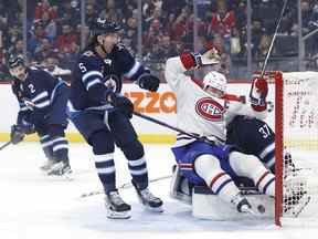 Le centre des Canadiens de Montréal Nick Suzuki (14) se glisse dans le gardien des Jets de Winnipeg Connor Hellebuyck (37) après son but en première période.