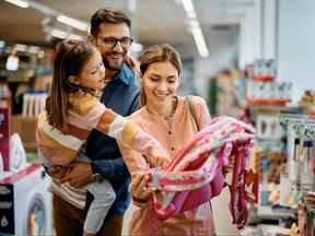 Bonne petite fille pointant vers le sac à dos tout en achetant des fournitures scolaires avec ses parents au supermarché.