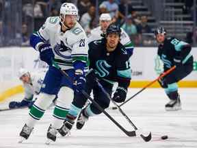 Le défenseur des Canucks de Vancouver Oliver Ekman-Larsson (23 ans) patine avec la rondelle contre l'ailier gauche de Seattle Kraken Brandon Tanev (13 ans) au Climate Pledge Arena.