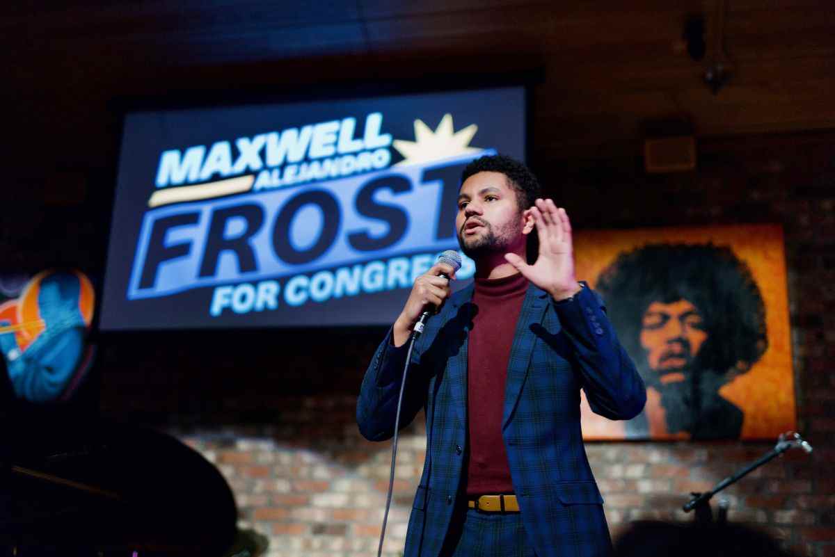 Maxwell Frost speaking on stage in a blue suit, gesturing with left hand